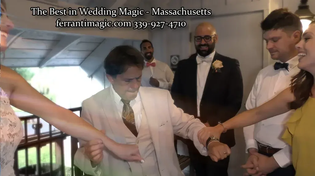 The Magic of Joe Ferranti Wedding party in formal attire watches a man in a cream suit perform a magic trick as guests link arms nearby in a corridor